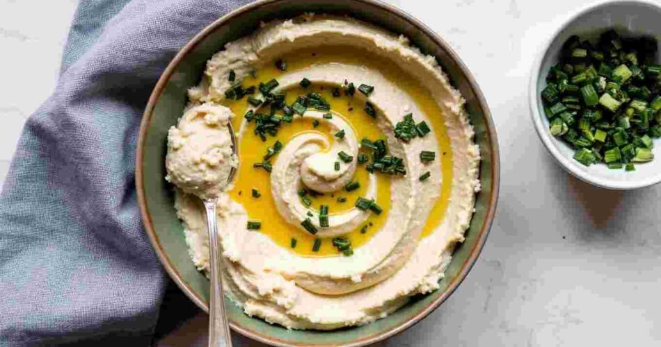 A bowl of green wild garlic hummus with olive oil and a leaf on top.